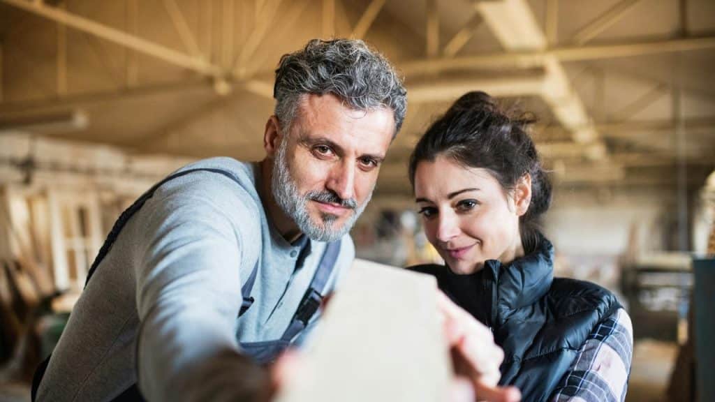 A man and a woman examining a wooden plank in a workshop.