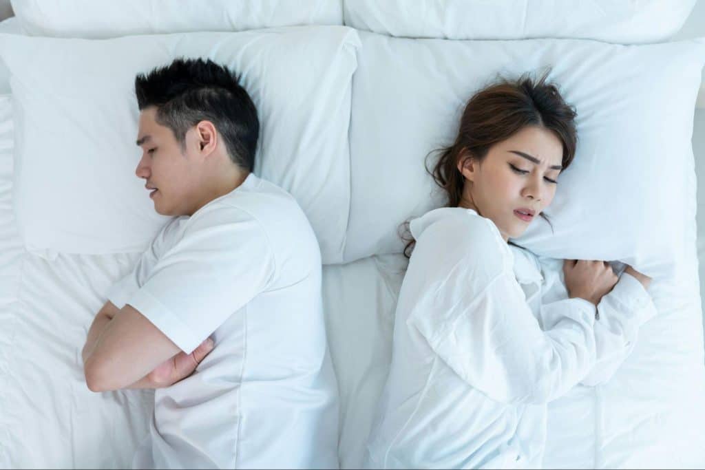 A couple facing away from each other while on the bed