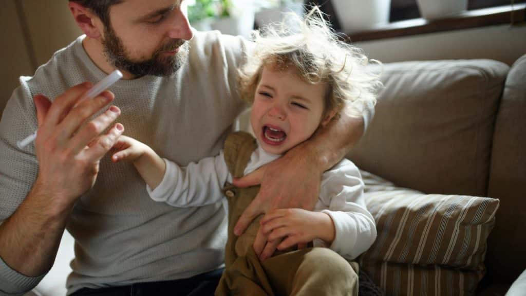 A father holding a syringe while his child cries.
