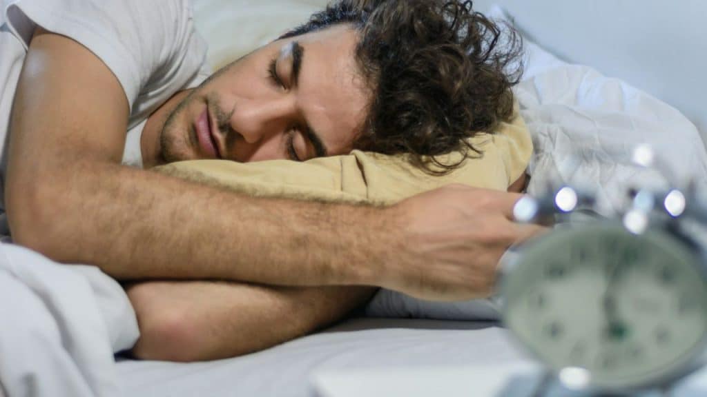 A man with dark, curly hair is sleeping peacefully on his side in bed.