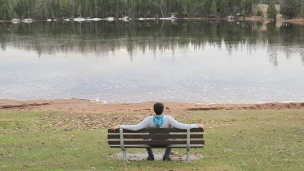 Man sitting on a bench in nature practicing mindful breathing.