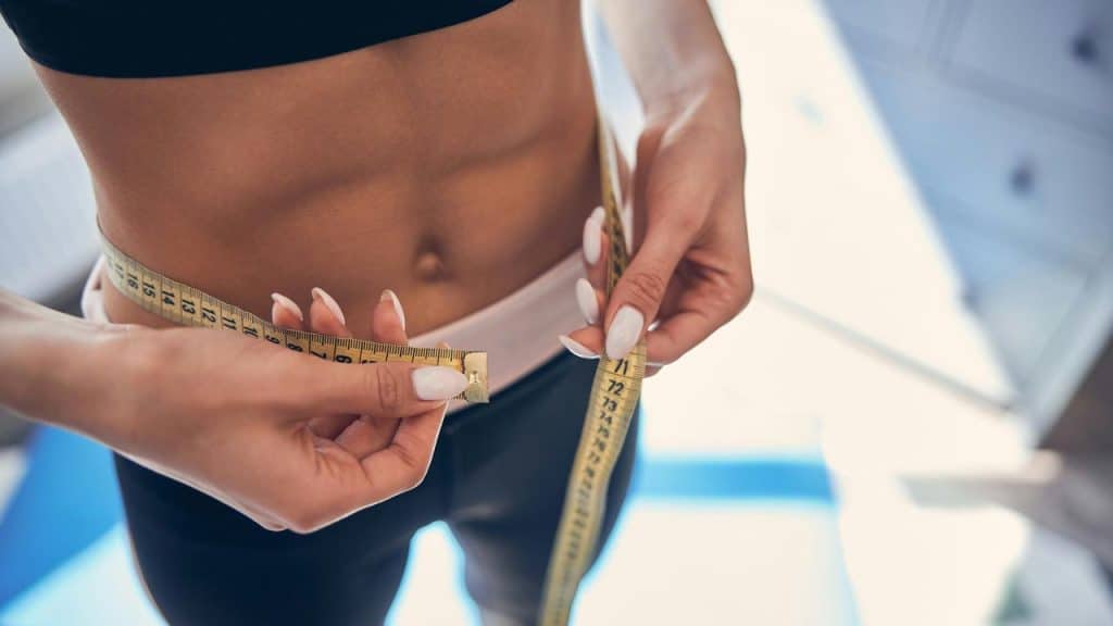 A person measuring a toned waist with a yellow tape measure.