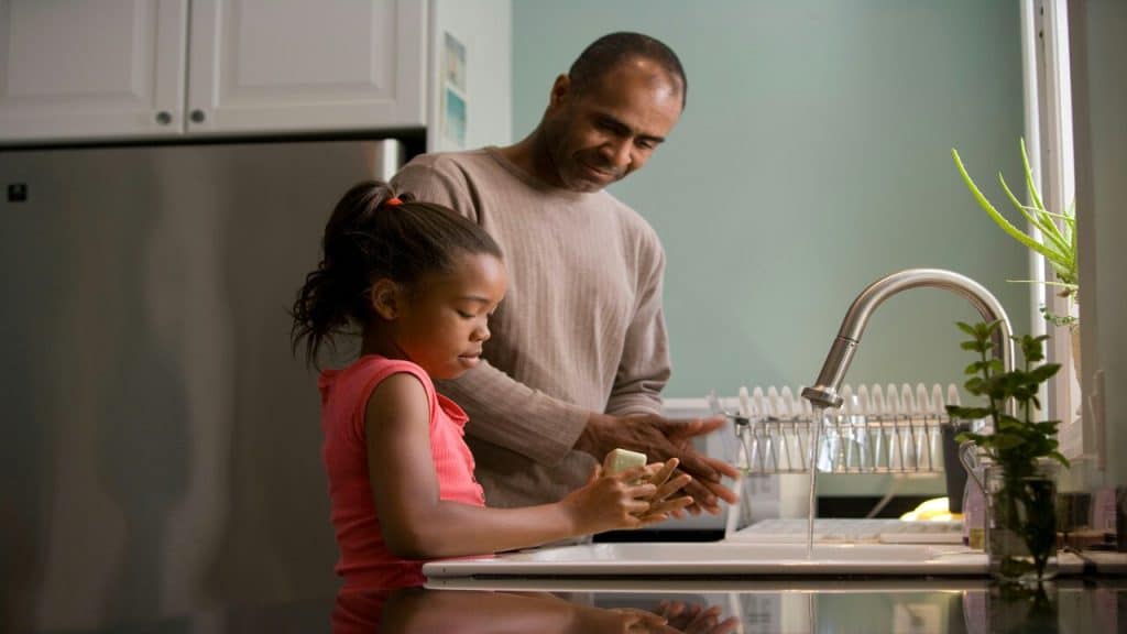 A dad helping his daughter wash her hands