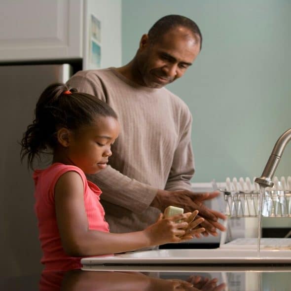 A dad helping his daughter wash her hands