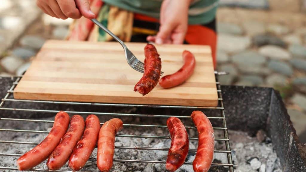 A fork lifting a sausage from a charcoal grill.