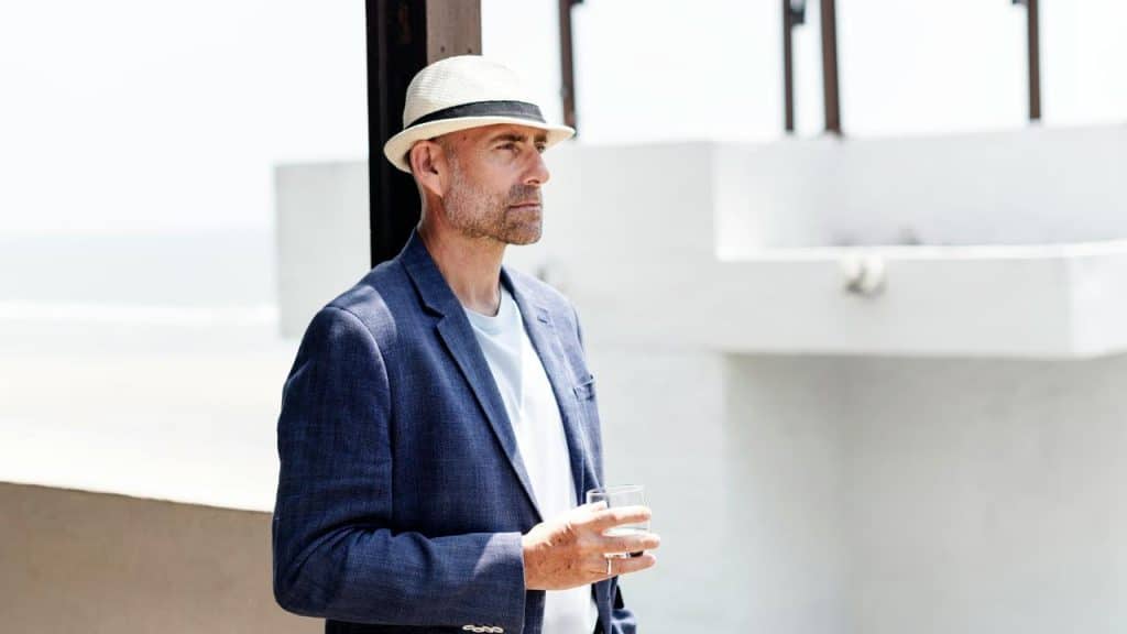 A man in a hat holding a glass outdoors.