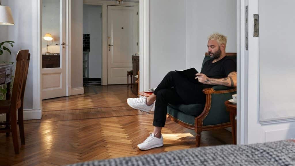 A man with bleached hair sits in a comfortable armchair, reading a book.