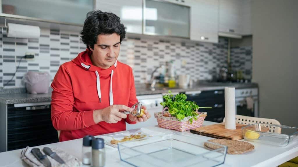 A man in a red hoodie peels potatoes at a kitchen table.