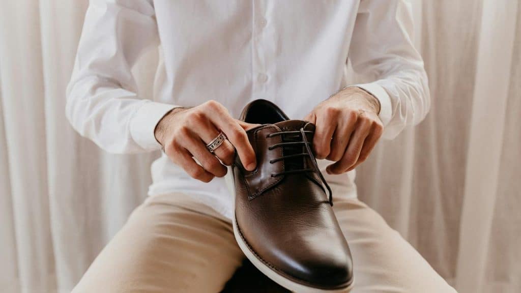 A person’s hands tying the laces of a brown leather dress shoe.