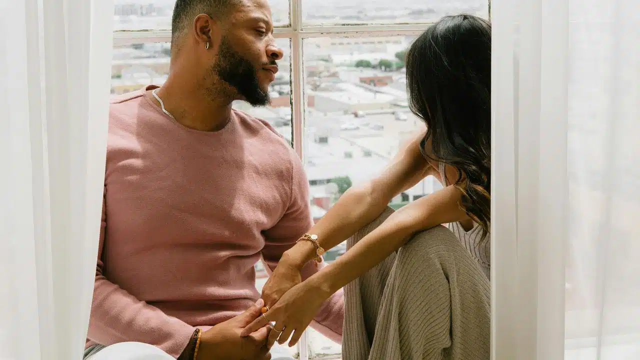 A couple holding hands while sitting by a window.