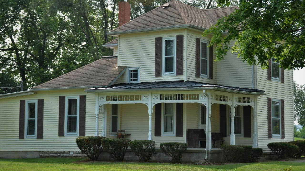 A large, two-story yellow house with brown shutters and a front porch.