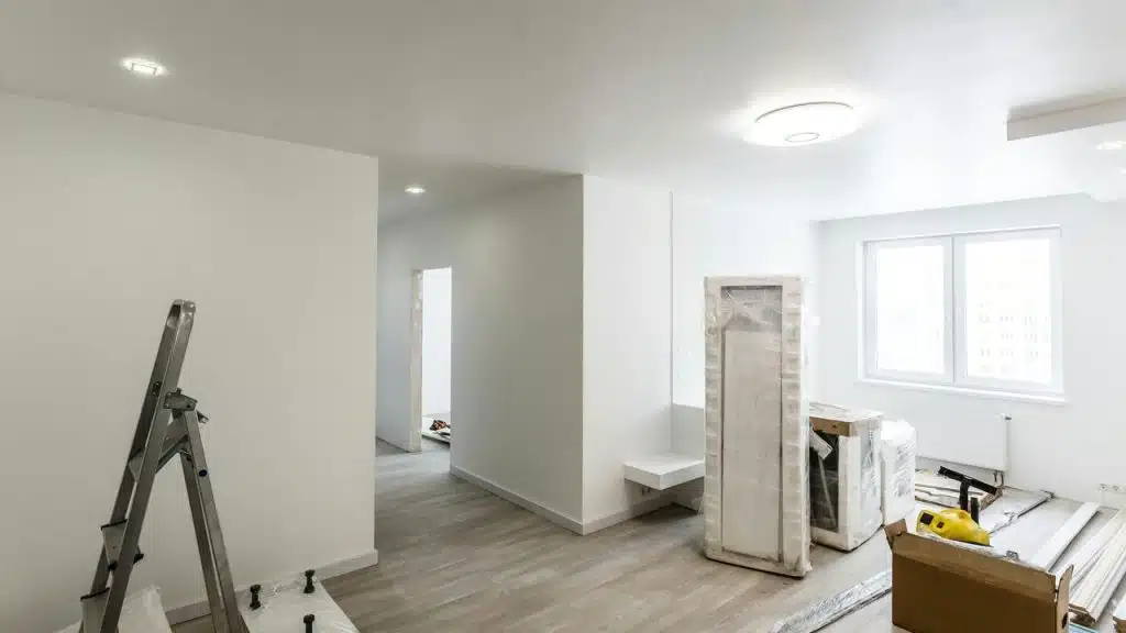 An unfinished white room with a ladder, wrapped furniture, and boxes.