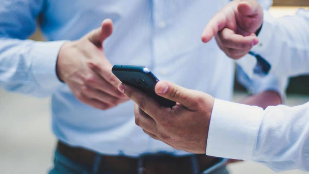 A close-up of hands holding a smartphone while another person points.