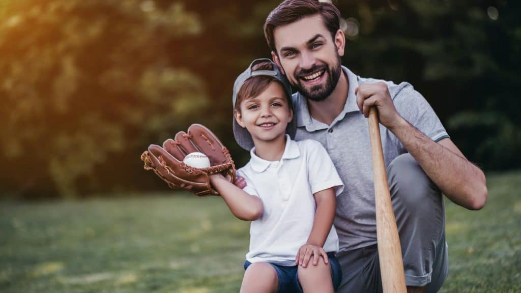 A man kneeling beside a boy holding a baseball glove and bat.