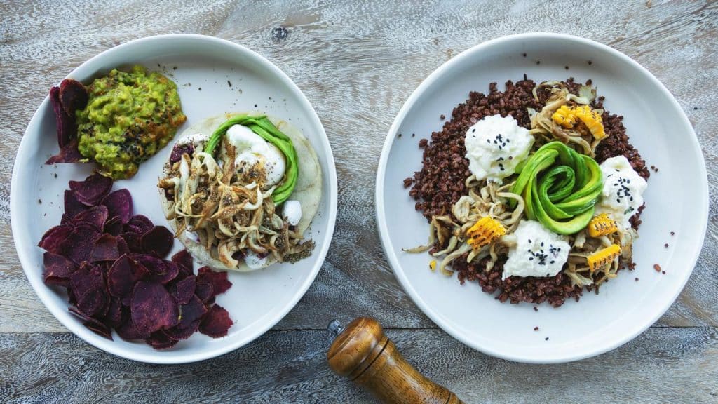A pair of plant bowls with avocado, mushrooms, grains, and beet chips.