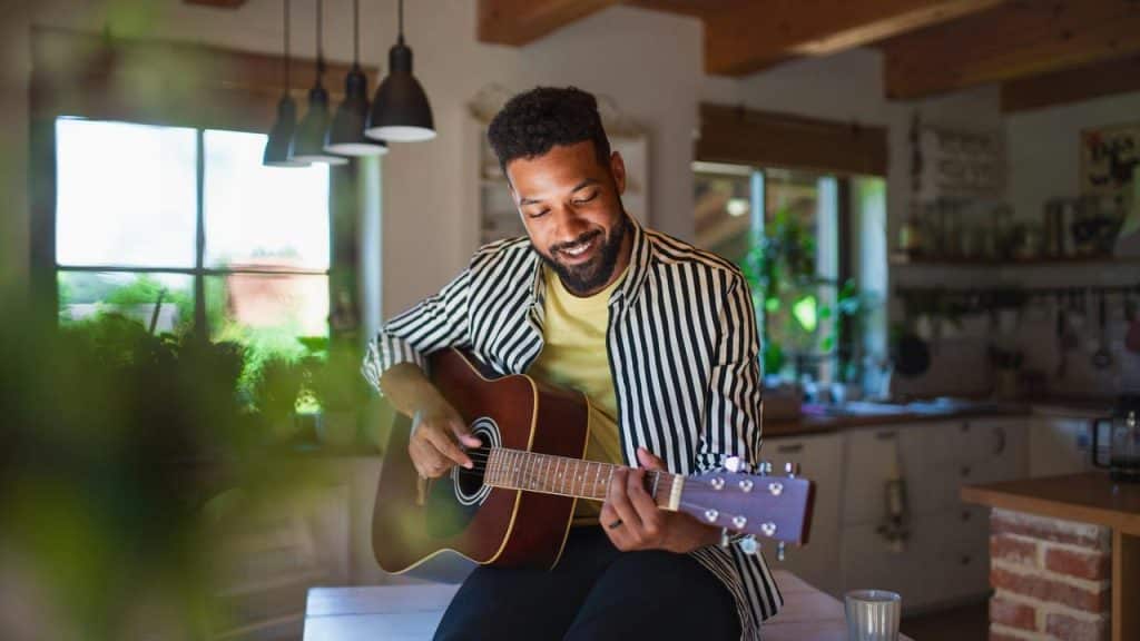 A man strumming an acoustic guitar in a bright kitchen.