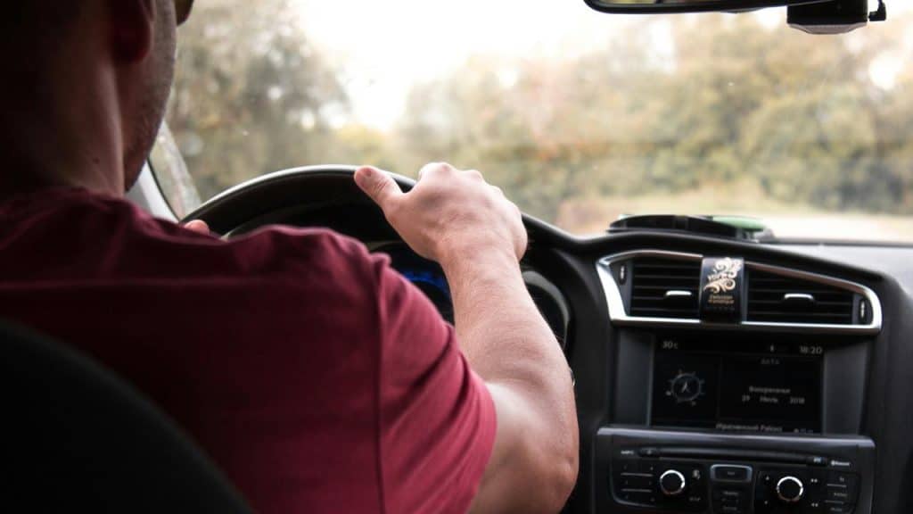A driver’s hands on a steering wheel with the car dashboard in view.