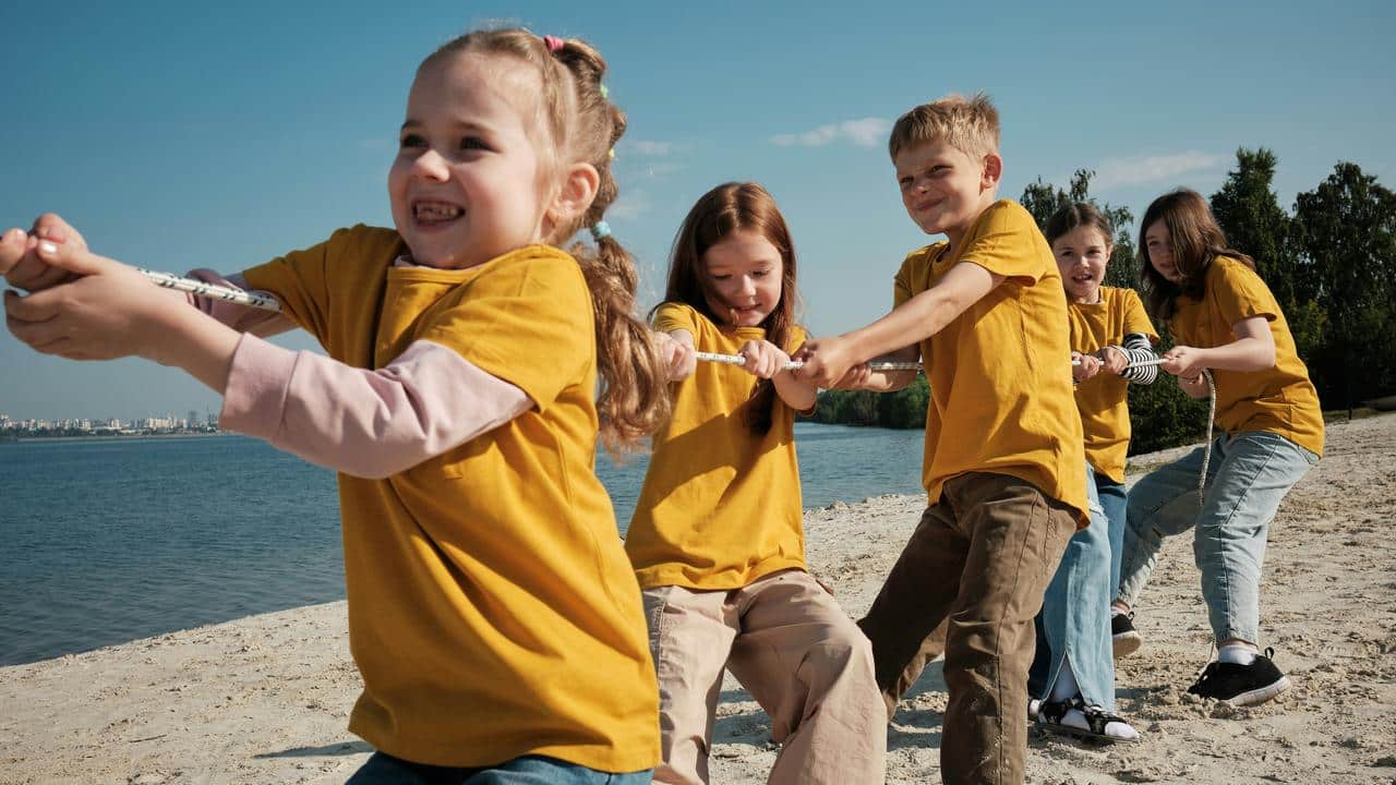 A group of children playing tug‑of‑war on a beach.