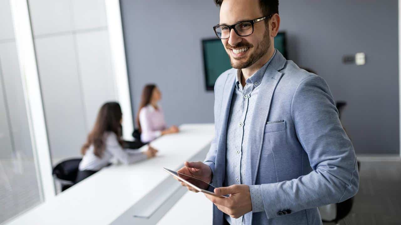 A smiling man holding a tablet in an office.