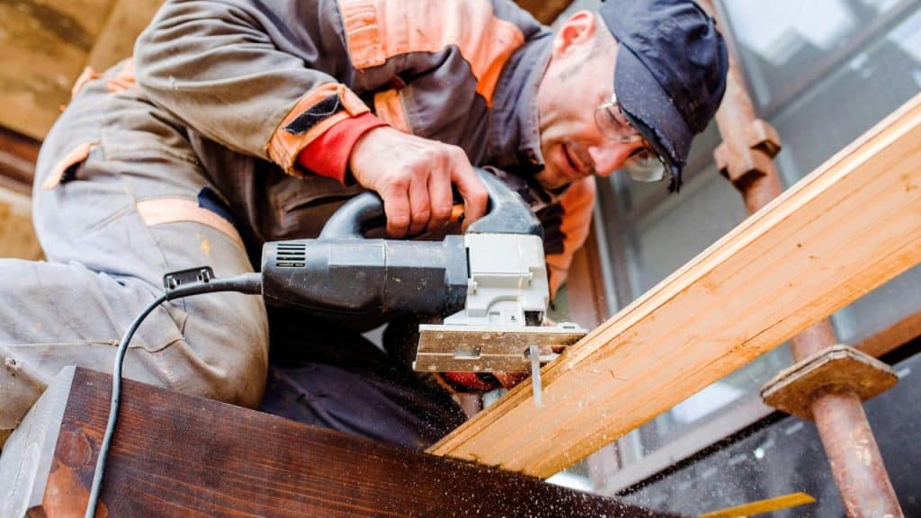 A construction worker using an electric jigsaw to cut wood.