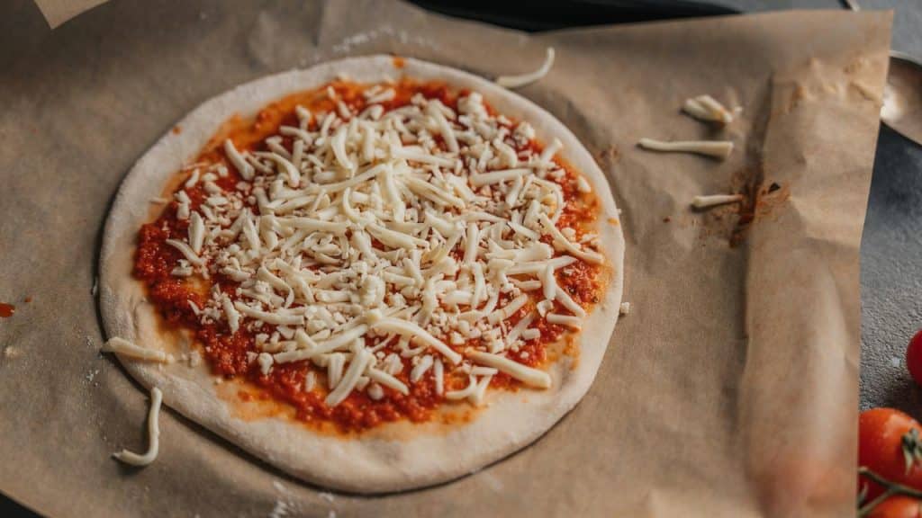 A pizza crust spread with tomato sauce and shredded cheese.