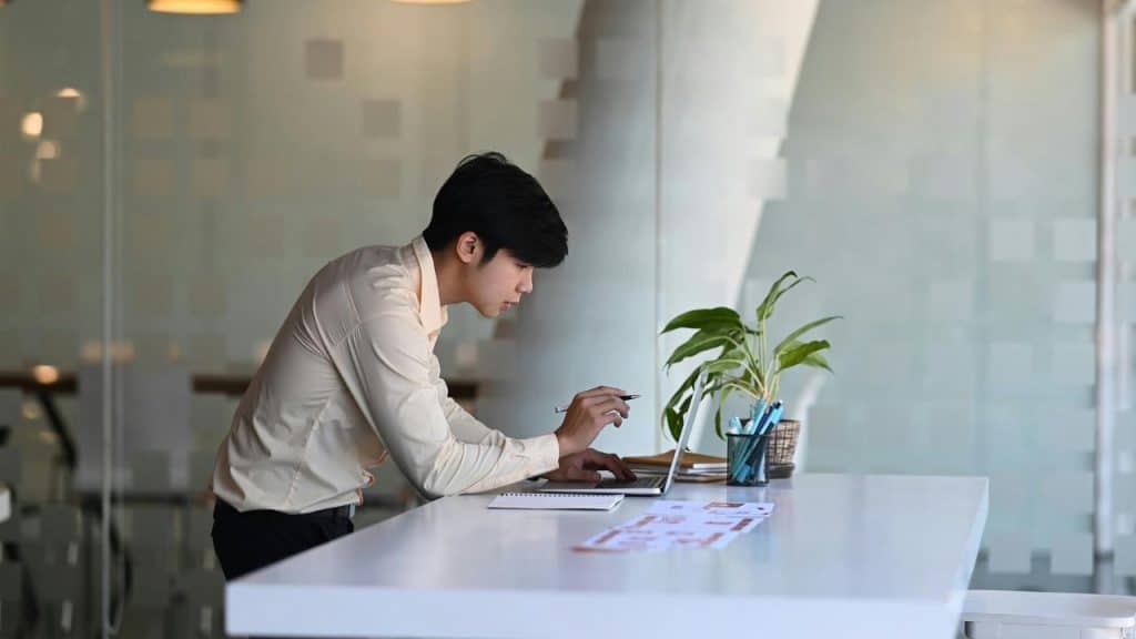 A man leaning over a desk to point at a laptop.