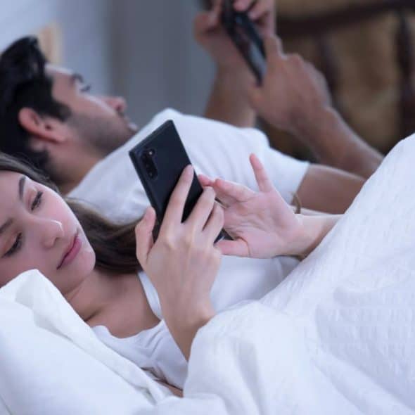 A couple lying in bed looking at their smartphones.