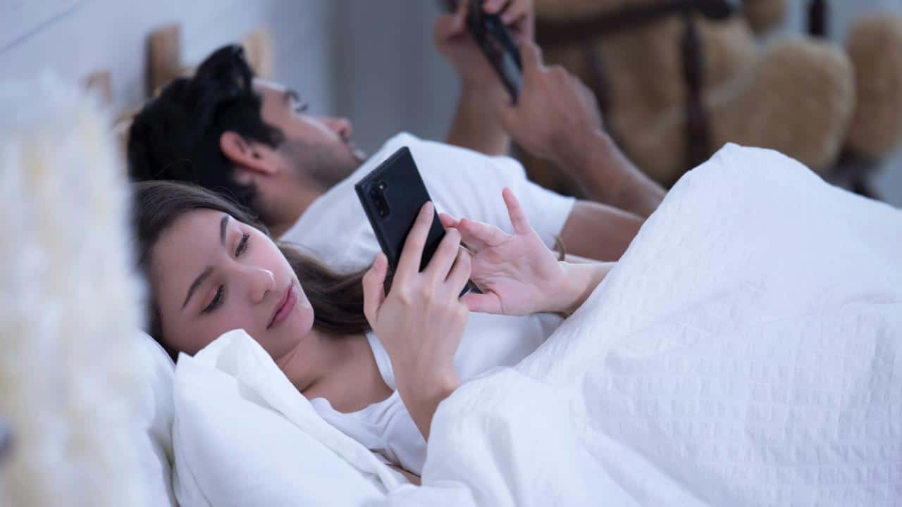 A couple lying in bed looking at their smartphones.