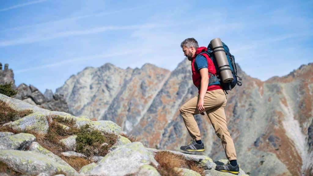 A man with a large backpack hikes up a rocky mountain with a blue sky.