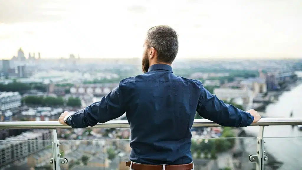 A man from behind looks out over a city from a balcony.