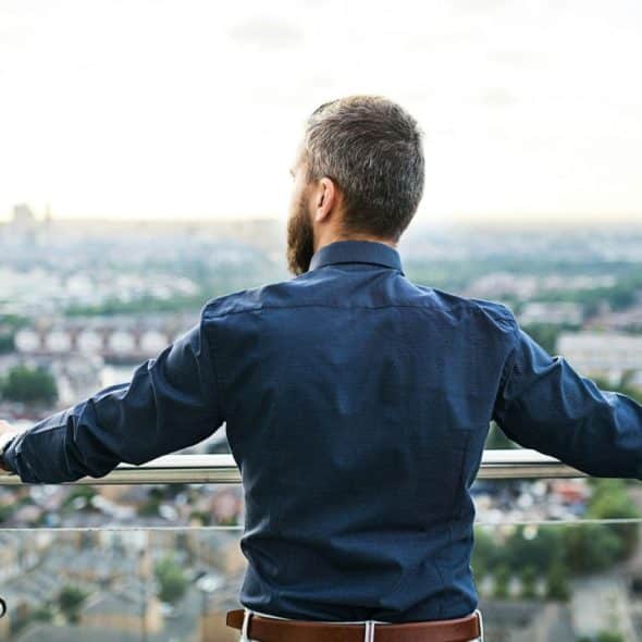 A man from behind looks out over a city from a balcony.