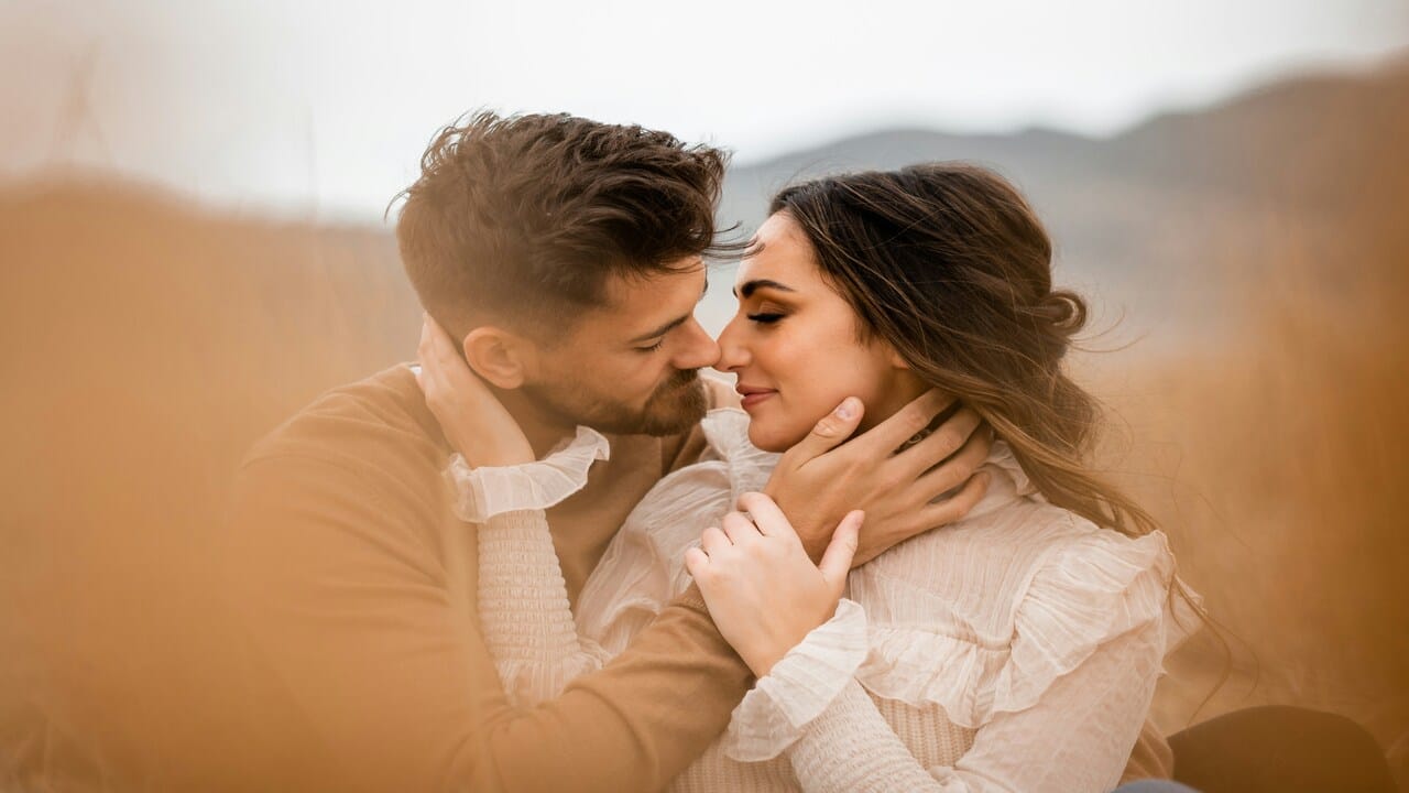 A couple almost kissing on a field.