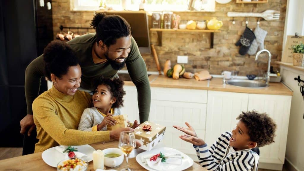 A family exchanging gifts around a kitchen table.