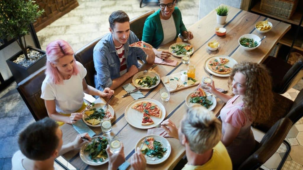 A group of friends eating pizza and salad around a wooden dining table.