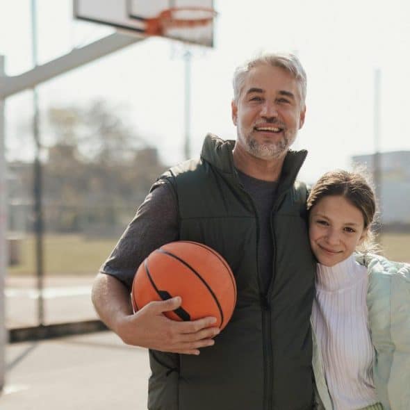 A man with a basketball and his daughter on an outdoor court.