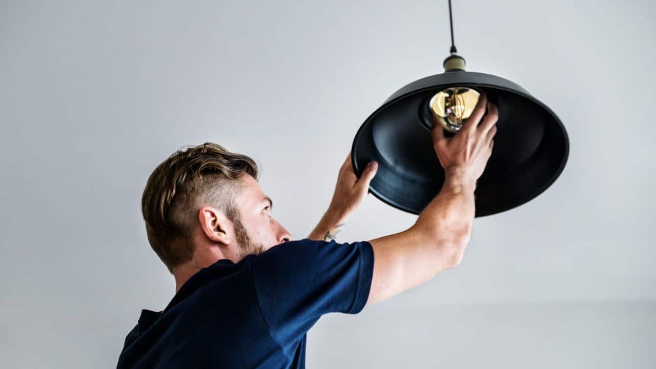 A man installs a light bulb into a black hanging lamp.