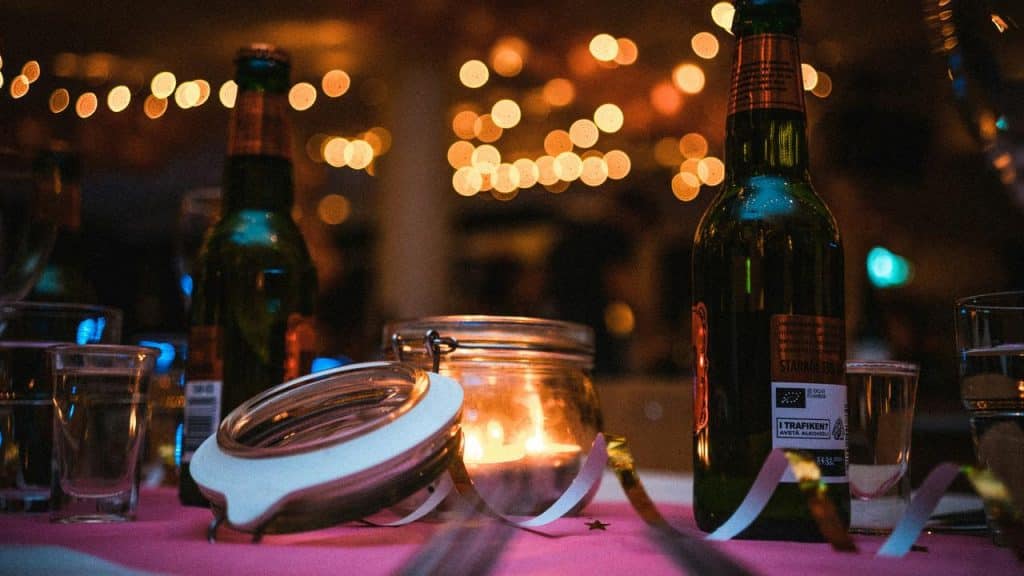 A candlelit jar on a party table surrounded by beer bottles and shot glasses.