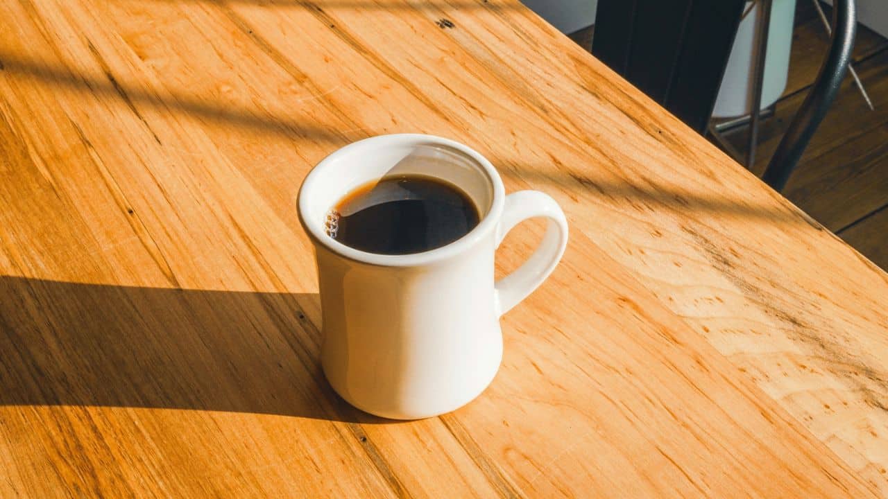 A white coffee mug filled with dark liquid sits on a wooden table.