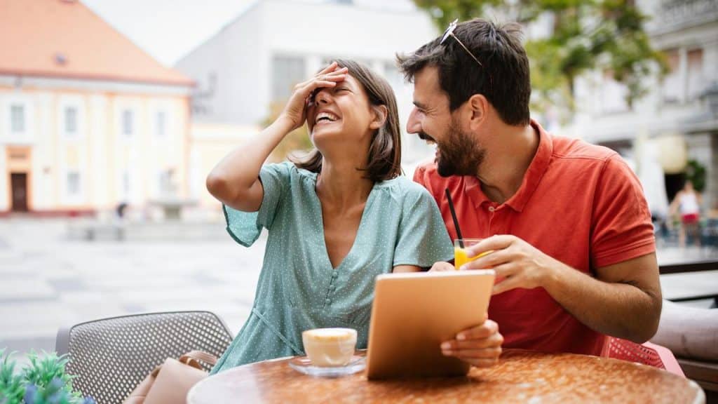 A woman laughing while holding a tablet next to a man with a drink.