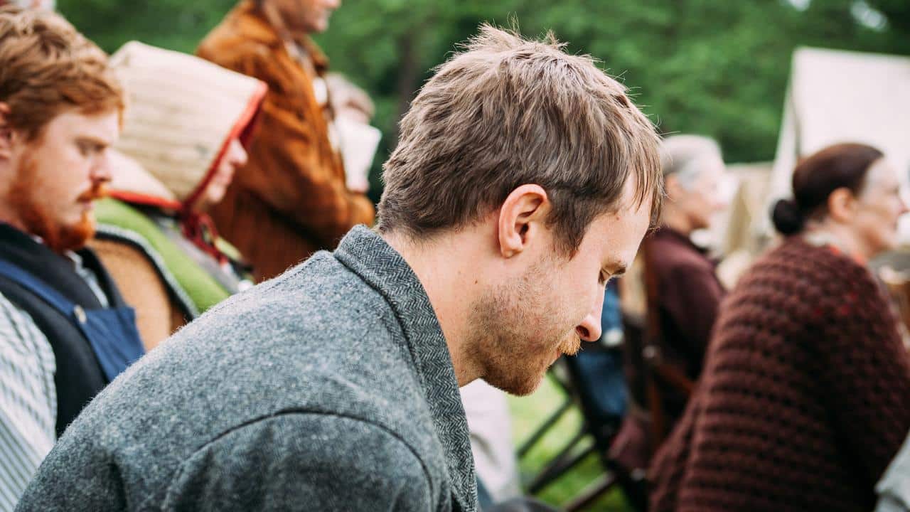A man seated at an outdoor gathering, looking down.
