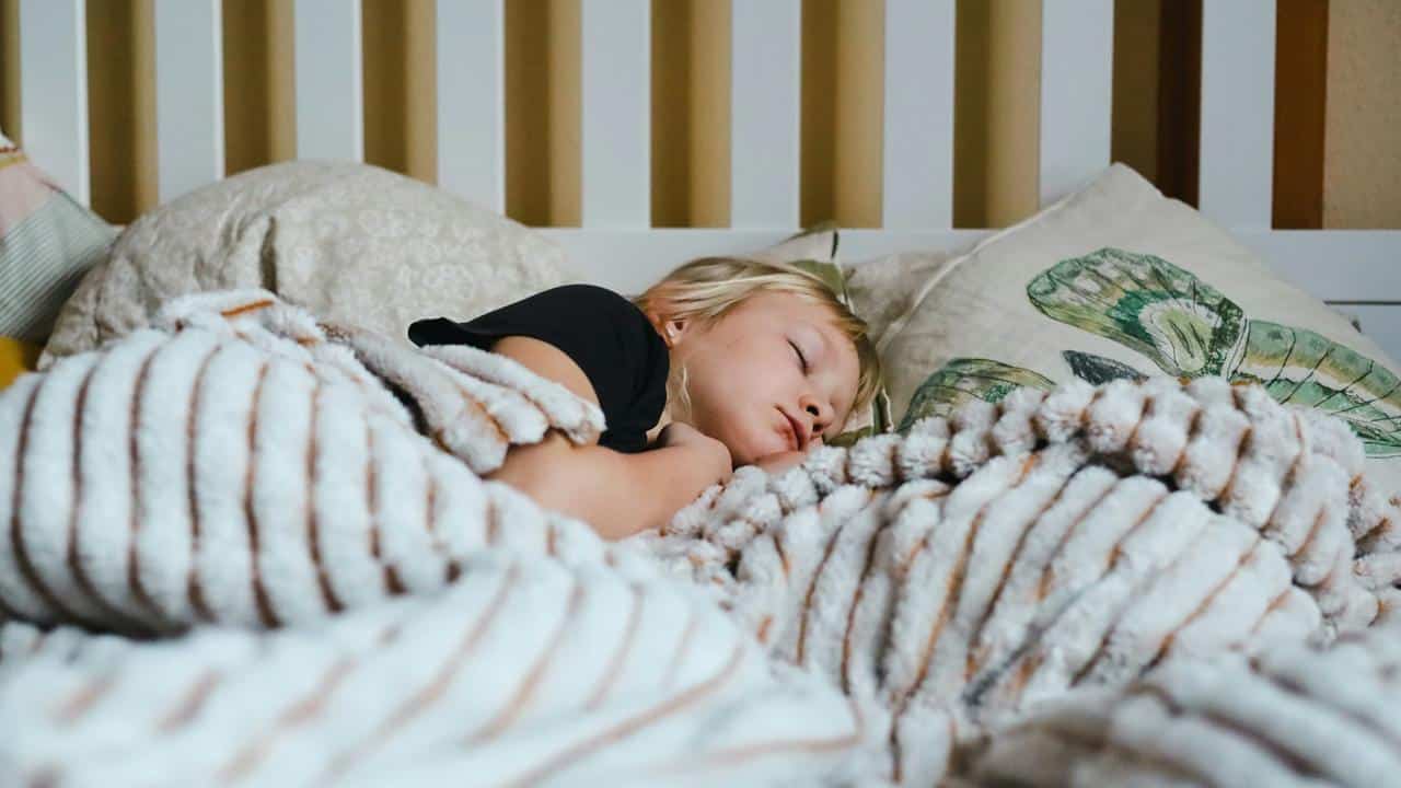A child sleeping under a striped blanket in a bed.