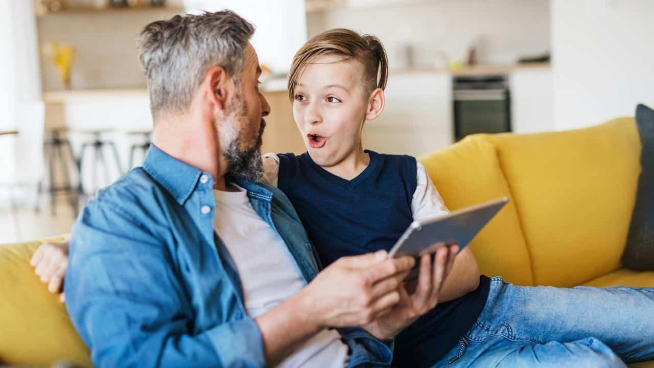 A father and son on a couch looking surprised at a tablet.