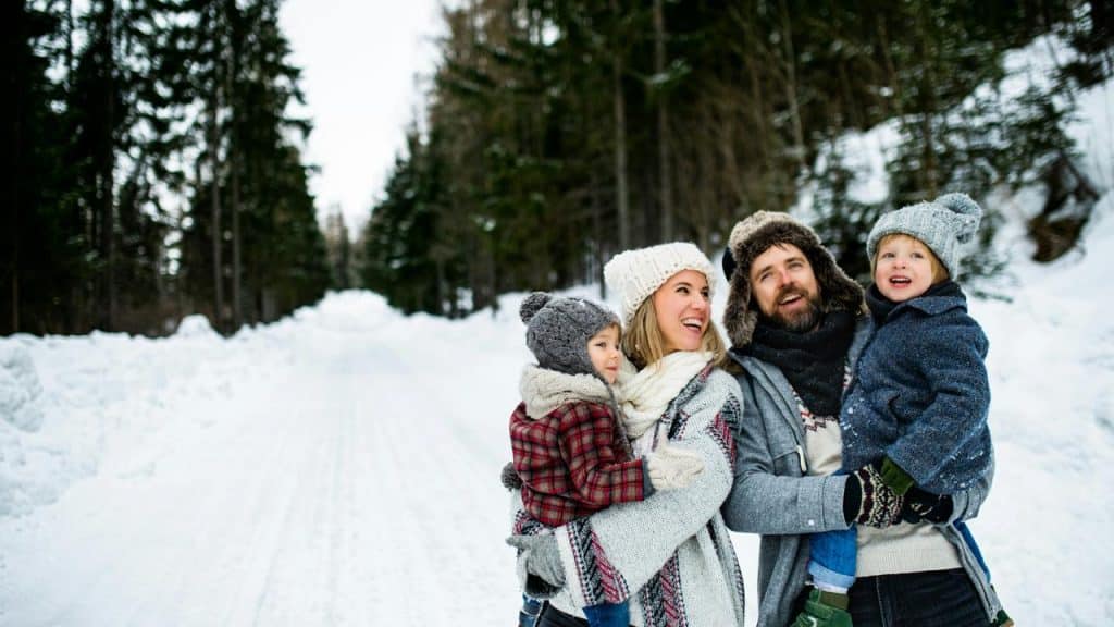 A family of two adults holding two children on a snowy forest road.