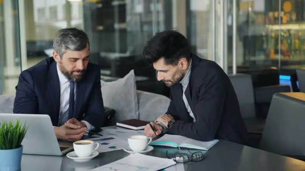 A pair of businessmen reviewing charts over coffee.