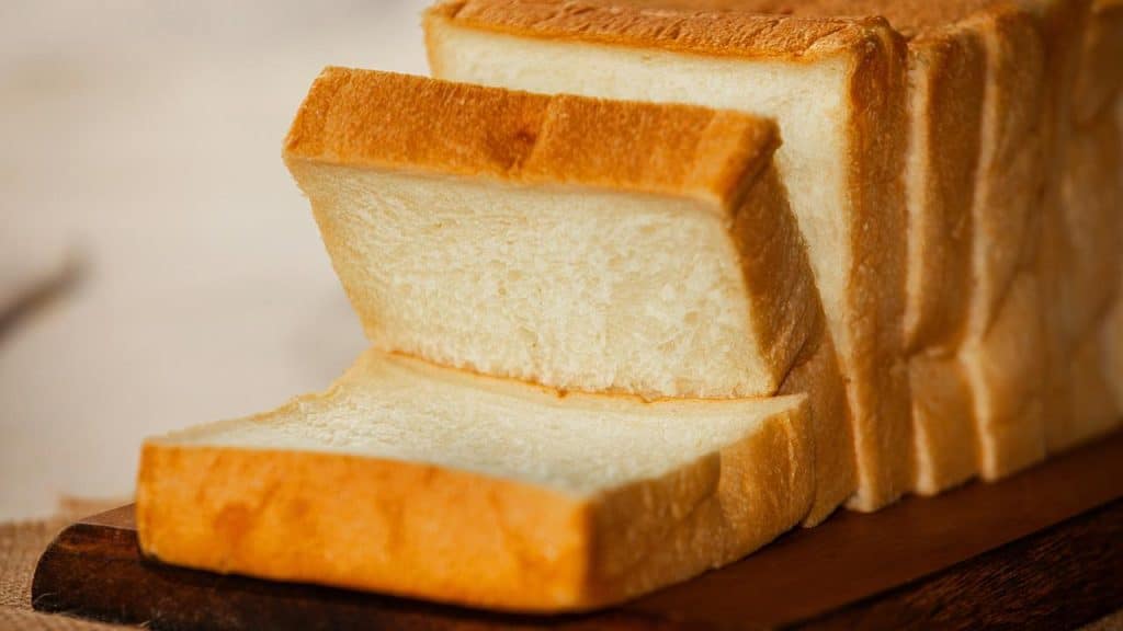 A sliced loaf of white bread on a wooden board.