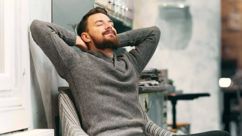 A bearded man leans back in a chair, eyes closed, appearing relaxed.