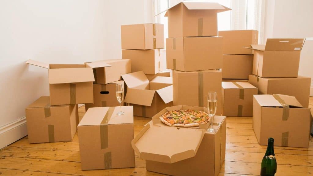 A pizza and two glasses of champagne amid unpacked moving boxes.