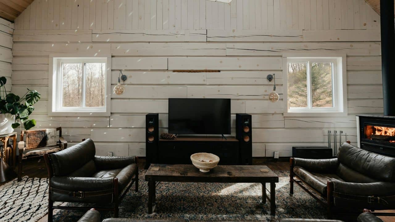 A living room with light wooden walls, a large TV, two armchairs, and a fireplace.