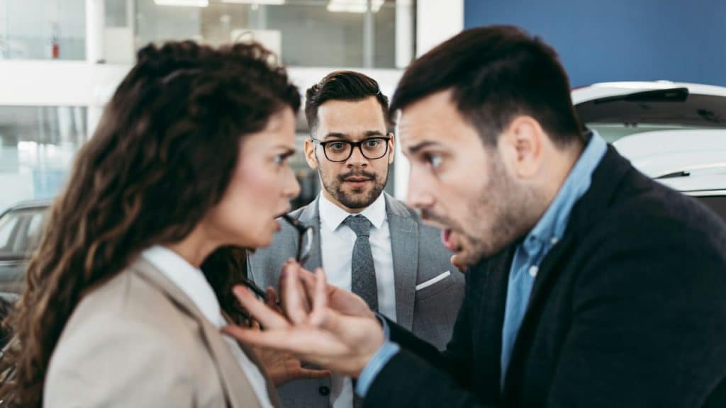 A man and woman argue while another man in glasses looks on in the background.