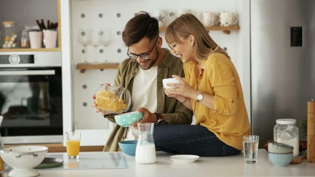 Man preparing breakfast for his partner with two bowls of cereal and milk